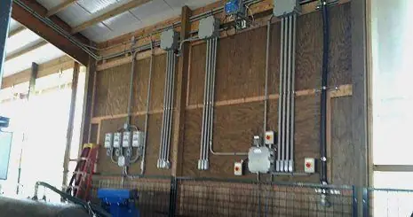 Conduit runs, panels and disconnects mounted on the wood-frame wall of an agricultural building wired by Bauer Electric
